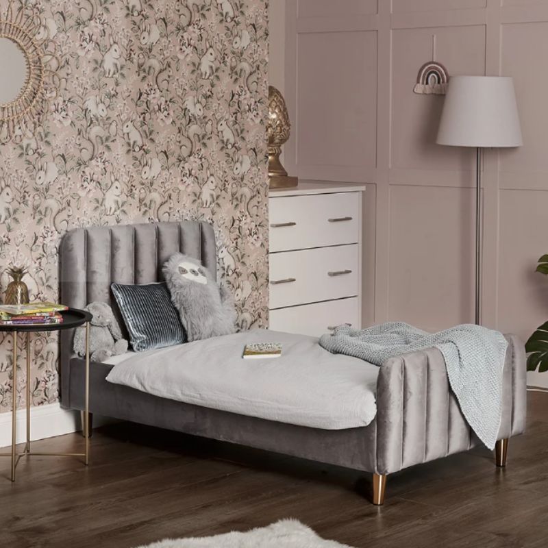 A modern single bed frame upholstered in gray velvet with vertical channel tufting on the headboard and footboard, supported by slim gold-toned legs, shown with a white mattress on a plain white background.