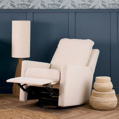 An upholstered recliner chair in a textured cream bouclé fabric, shown with the footrest extended in a styled room setting with a blue paneled wall, a floor lamp, and a decorative basket.