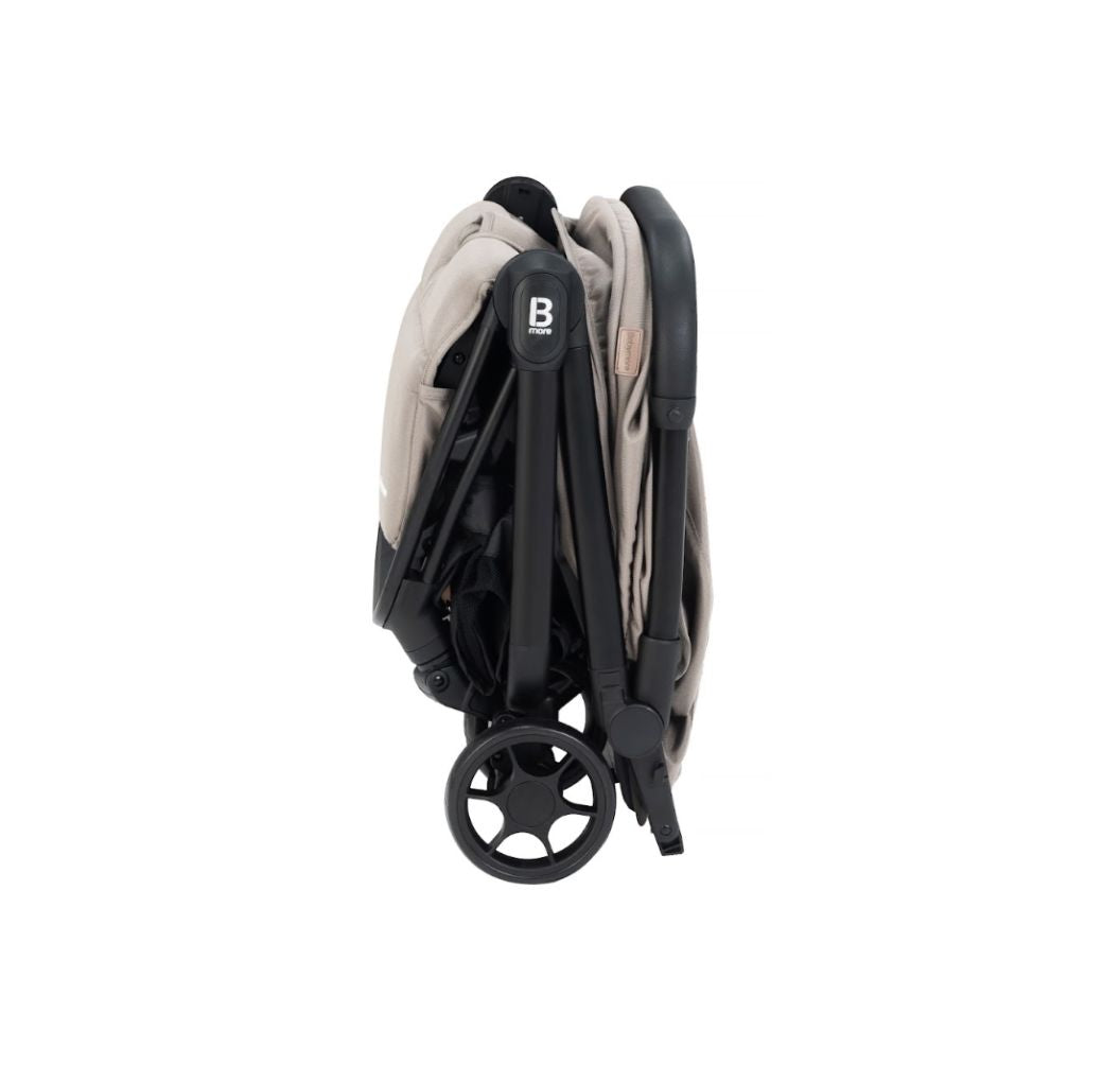 A compact stroller with a light beige (latte) canopy and seat liner, a black frame, and black wheels, shown from a three-quarters angle on a solid white background.