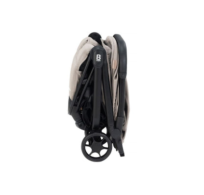 A compact stroller with a light beige (latte) canopy and seat liner, a black frame, and black wheels, shown from a three-quarters angle on a solid white background.