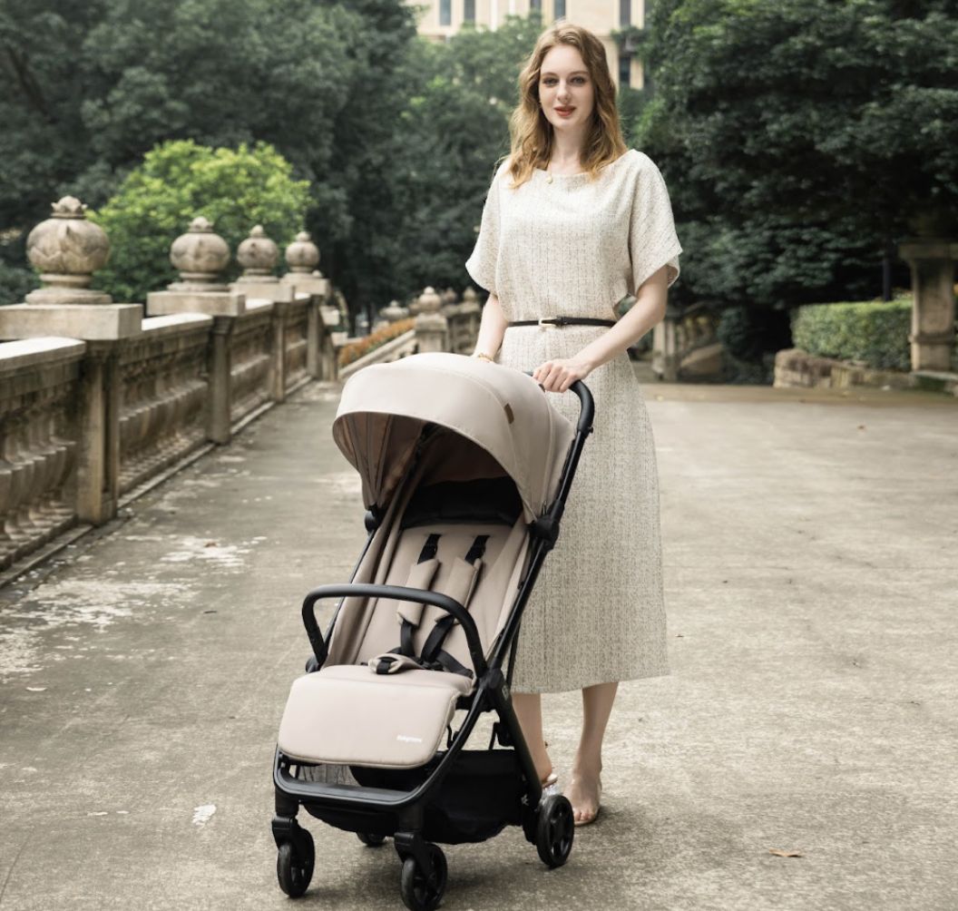 A compact stroller with a light beige (latte) canopy and seat liner, a black frame, and black wheels, shown from a three-quarters angle on a solid white background.