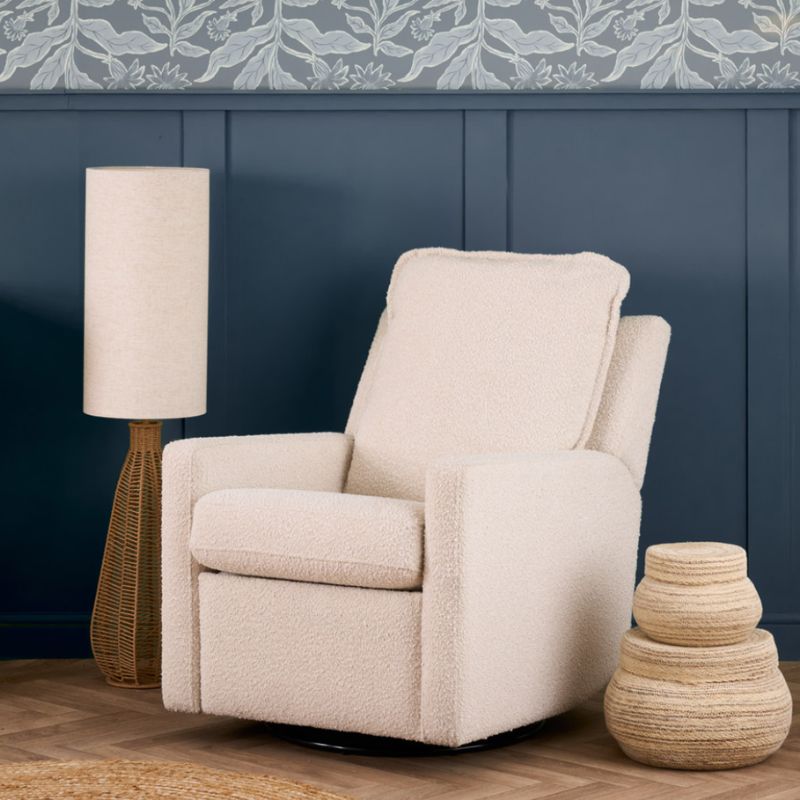 An upholstered recliner chair in a textured cream bouclé fabric, shown with the footrest extended in a styled room setting with a blue paneled wall, a floor lamp, and a decorative basket.