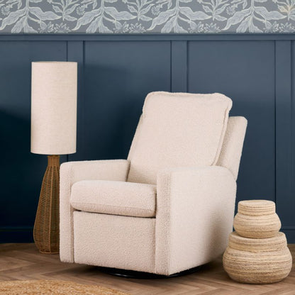 An upholstered recliner chair in a textured cream bouclé fabric, shown with the footrest extended in a styled room setting with a blue paneled wall, a floor lamp, and a decorative basket.