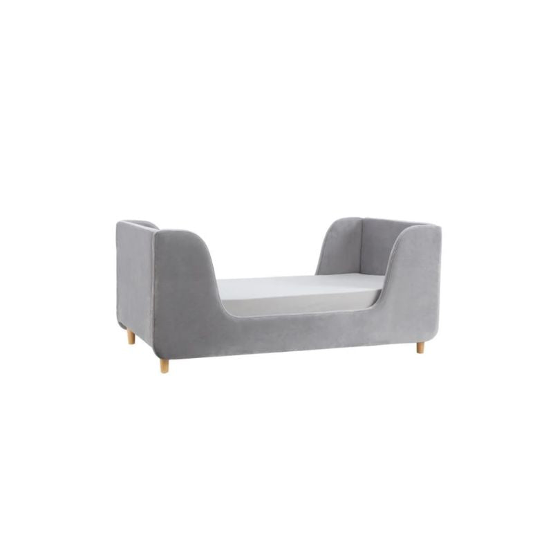A gray upholstered children's daybed in a styled nursery or playroom with teal paneled walls, a star wall decor piece, a window with bright sunlight, a bean bag, and a basket of toys.